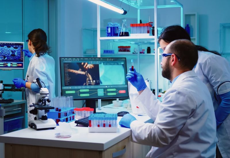 microbiologist-doctor-taking-blood-sample-tube-from-rack-with-machines-analysis-lab-background (1)