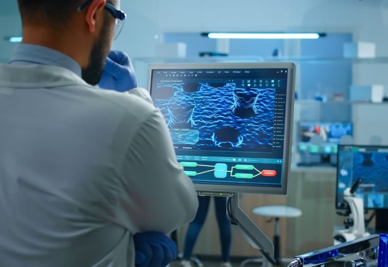 scientist-working-laboratory-analysing-test-trial-vaccine-checking-drug-data-standing-front-pc (1)